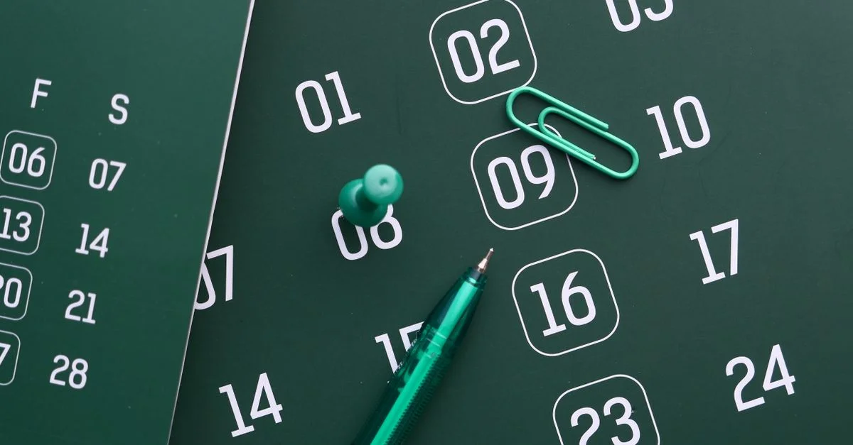 Gros plan sur un calendrier vert avec un stylo, une épingle et un trombone pour la planification et l'organisation.