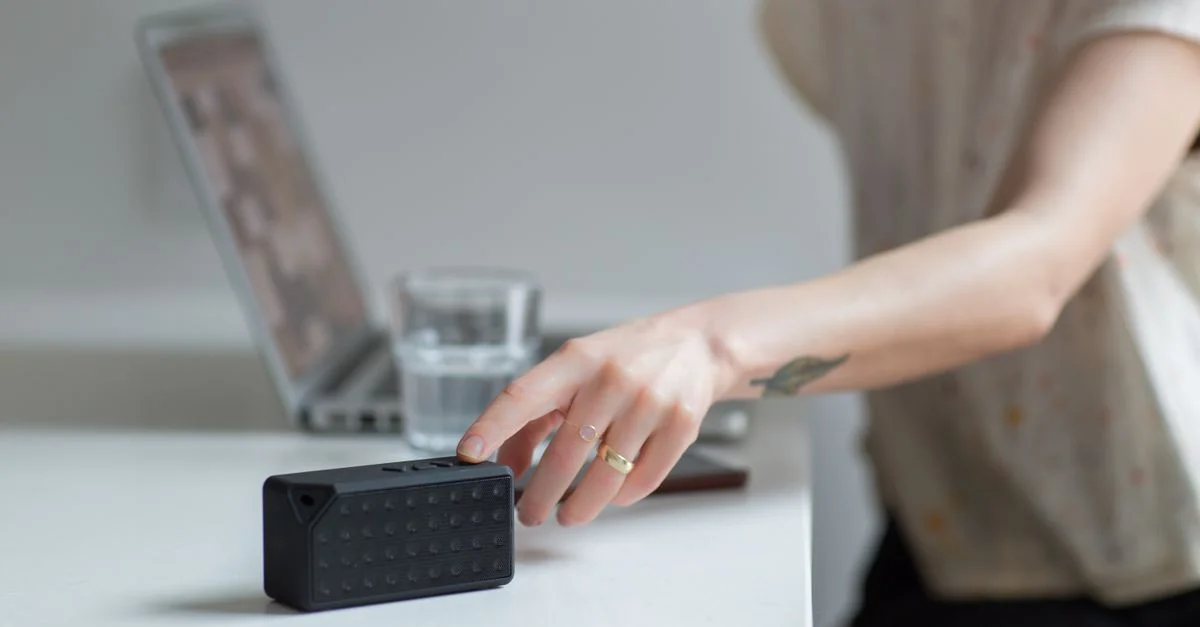 Gros plan sur une main atteignant un haut-parleur sans fil sur un bureau à côté d'un ordinateur portable.