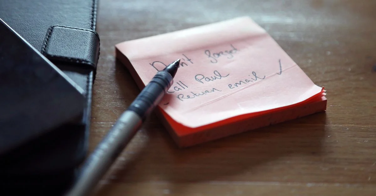Gros plan de notes autocollantes avec une liste de choses à faire, un stylo et un portefeuille sur un bureau en bois.