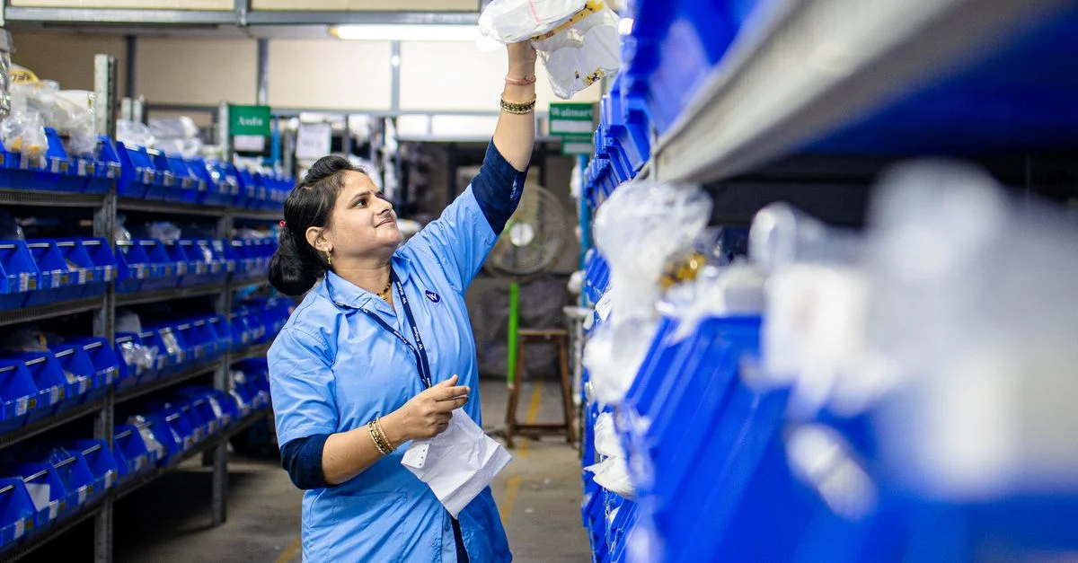 Une employée d'entrepôt organise les stocks sur des étagères industrielles bleues. Gestion logistique efficace.
