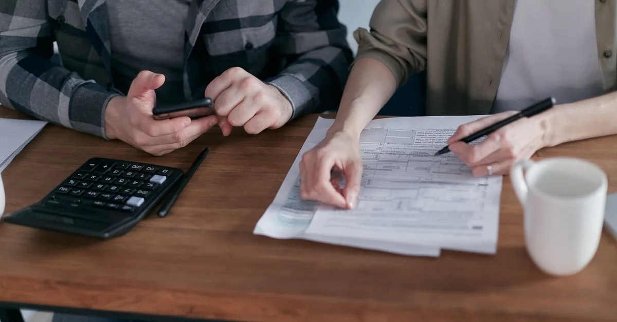 Un couple examine avec soin ses finances à l'aide d'une calculatrice et de documents à la maison.