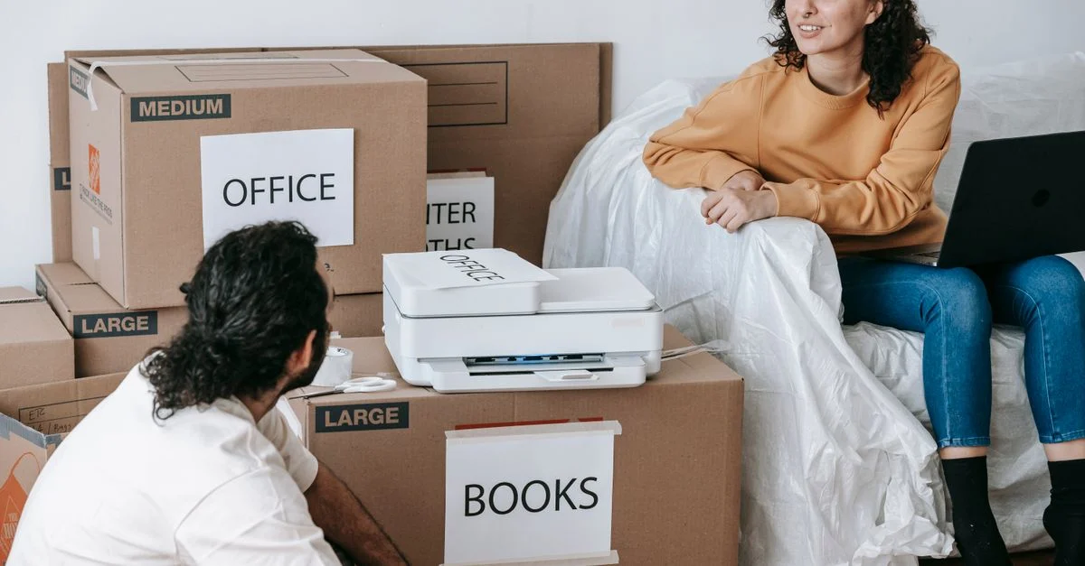 Jeune couple planifiant un déménagement avec des cartons emballés étiquetés pour l'organisation et un ordinateur portable pour la coordination.