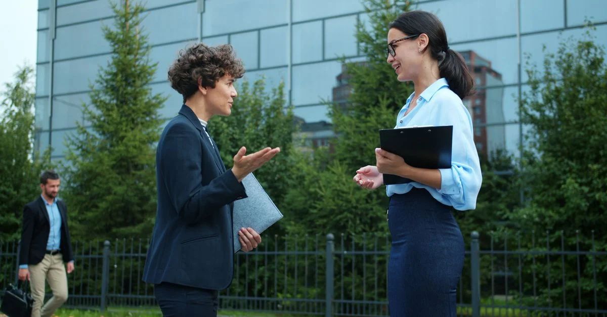 Deux professionnels ayant une discussion en extérieur près de bâtiments de bureaux.