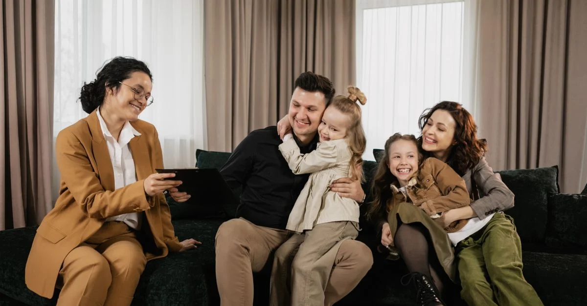 Une famille joyeuse assise dans le salon avec un agent immobilier discutant de l'achat d'une nouvelle maison.