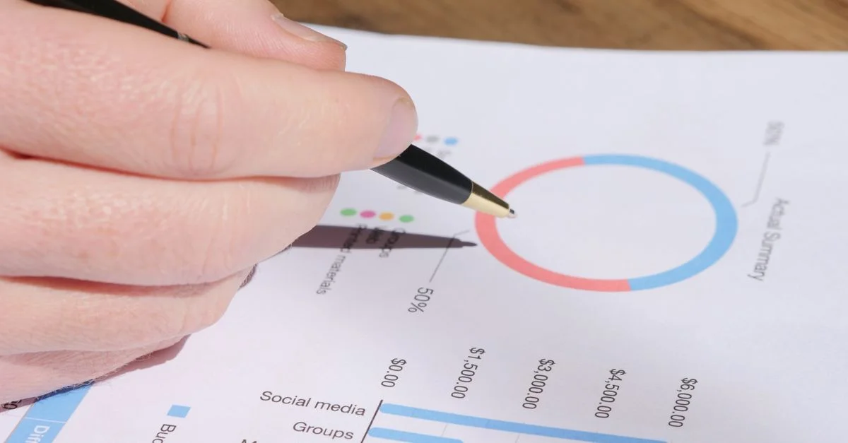 Une main avec un stylo examinant des graphiques et des tableaux d'affaires pour analyse.