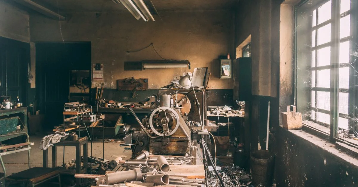 Atelier industriel rustique rempli de machines vintage, d'outils et de pièces en métal, situé dans une pièce faiblement éclairée.