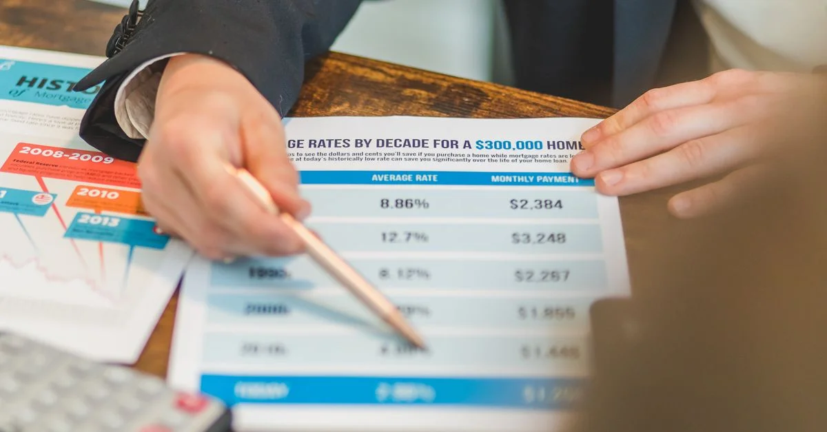Un gros plan de mains analysant des documents sur les taux hypothécaires avec un stylo et une calculatrice dans un cadre professionnel.