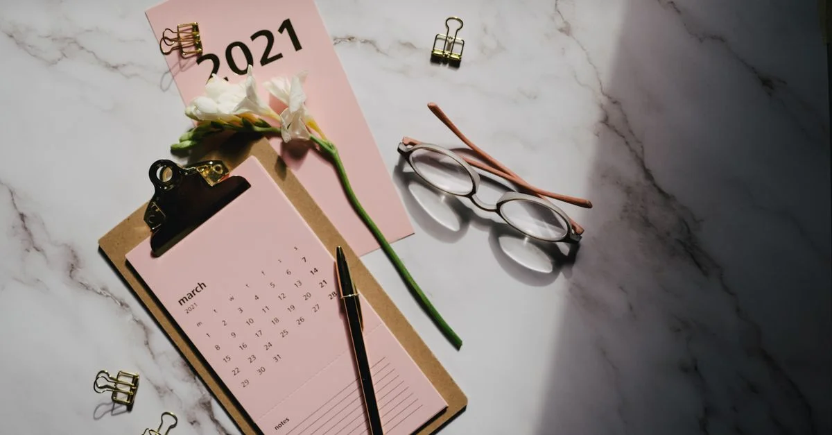 Élégante mise en scène à plat présentant un calendrier 2021, des lunettes et des fleurs blanches sur une surface en marbre.