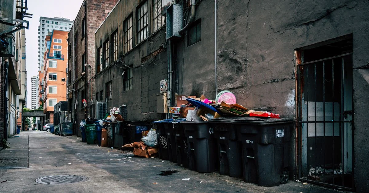 Une ruelle urbaine gritty à Seattle avec des bacs à ordures débordants et des immeubles de grande hauteur.