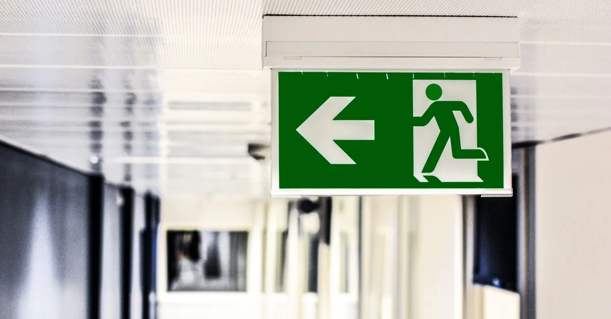 Panneau de sortie d'urgence vert avec flèche directionnelle dans un couloir.