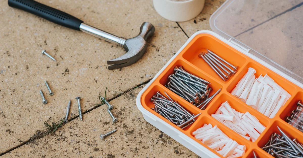 Vue de dessus d'un kit d'outils avec un marteau, des vis et des ancrages sur une surface en béton.