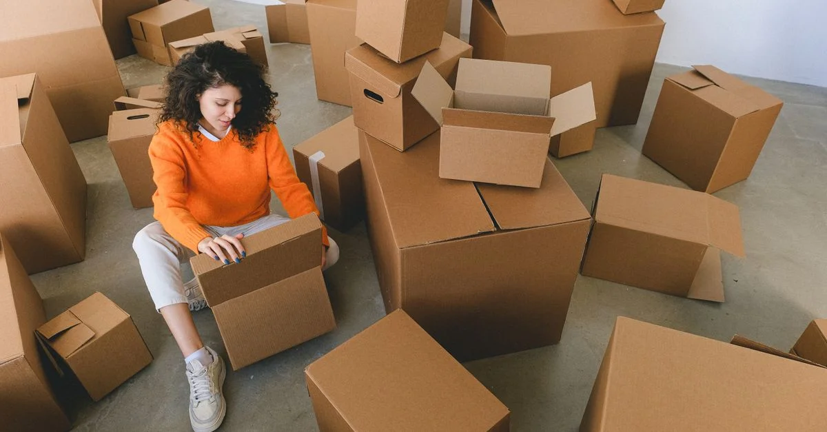 Une jeune femme aux cheveux frisés emballe des cartons dans son nouveau domicile, se préparant à déménager.