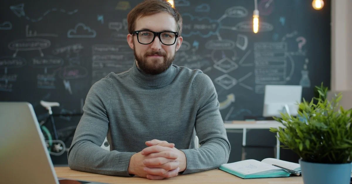 Professionnel sûr de lui, assis à un bureau dans un espace de travail moderne avec un tableau noir créatif en arrière-plan.