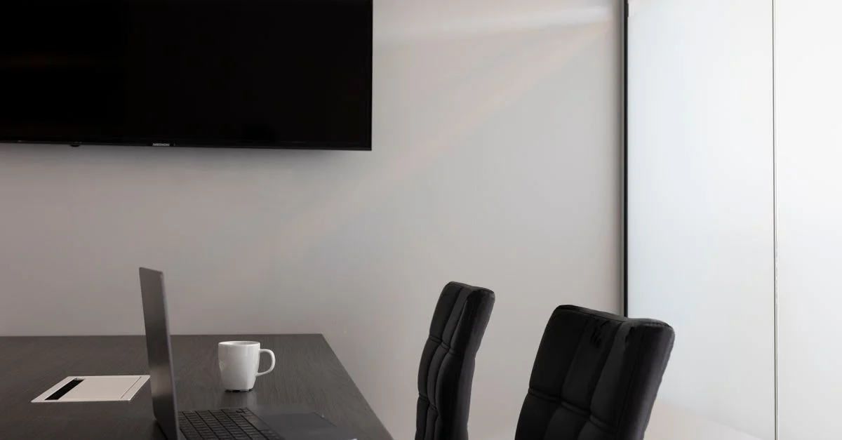 Un agencement de bureau moderne et élégant avec un ordinateur portable, une tasse et une télévision dans une salle de conférence vide.