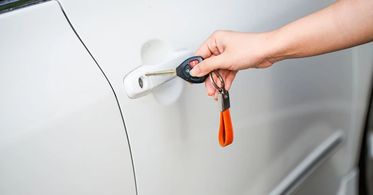 Gros plan d'une main déverrouillant une porte de voiture blanche avec une clé en métal et un porte-clé.