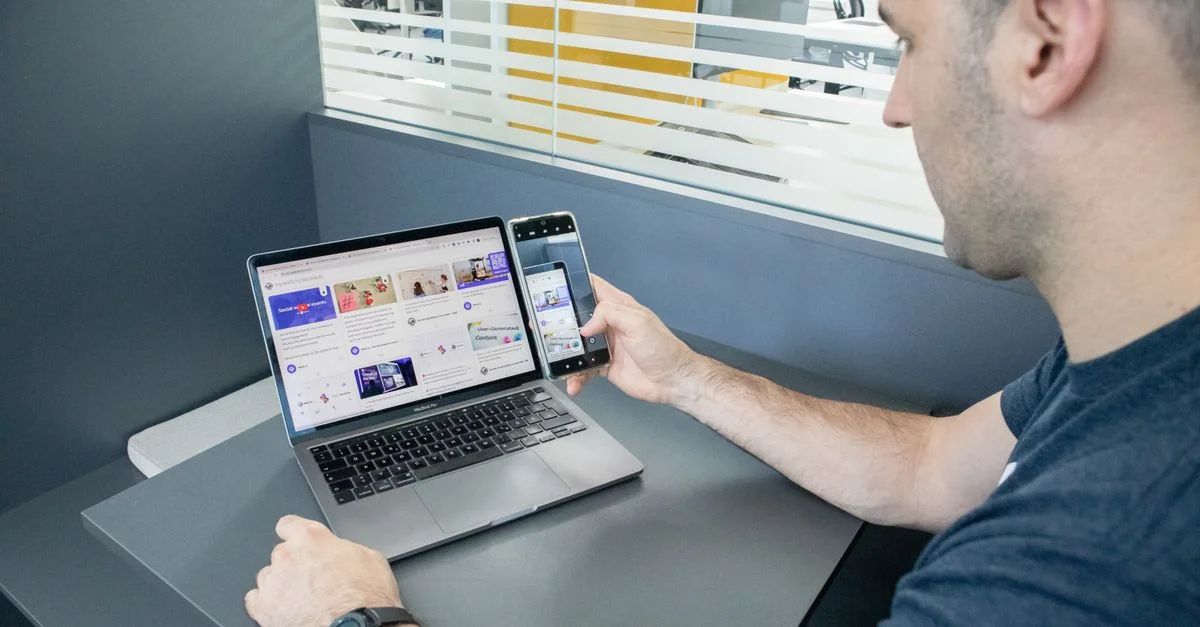 Un homme multitâche avec un portable et un smartphone dans un espace de bureau contemporain, illustrant l'utilisation de la technologie.