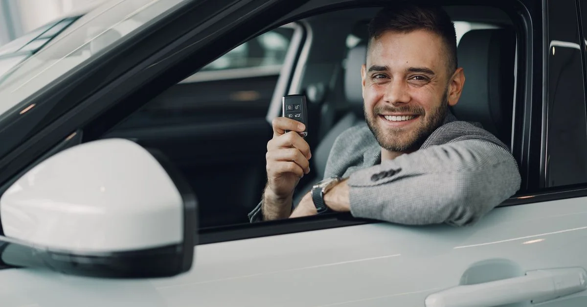 Jeune homme heureux tenant des clés de voiture à l'intérieur d'un véhicule. Image parfaite pour la location ou la vente de voitures.