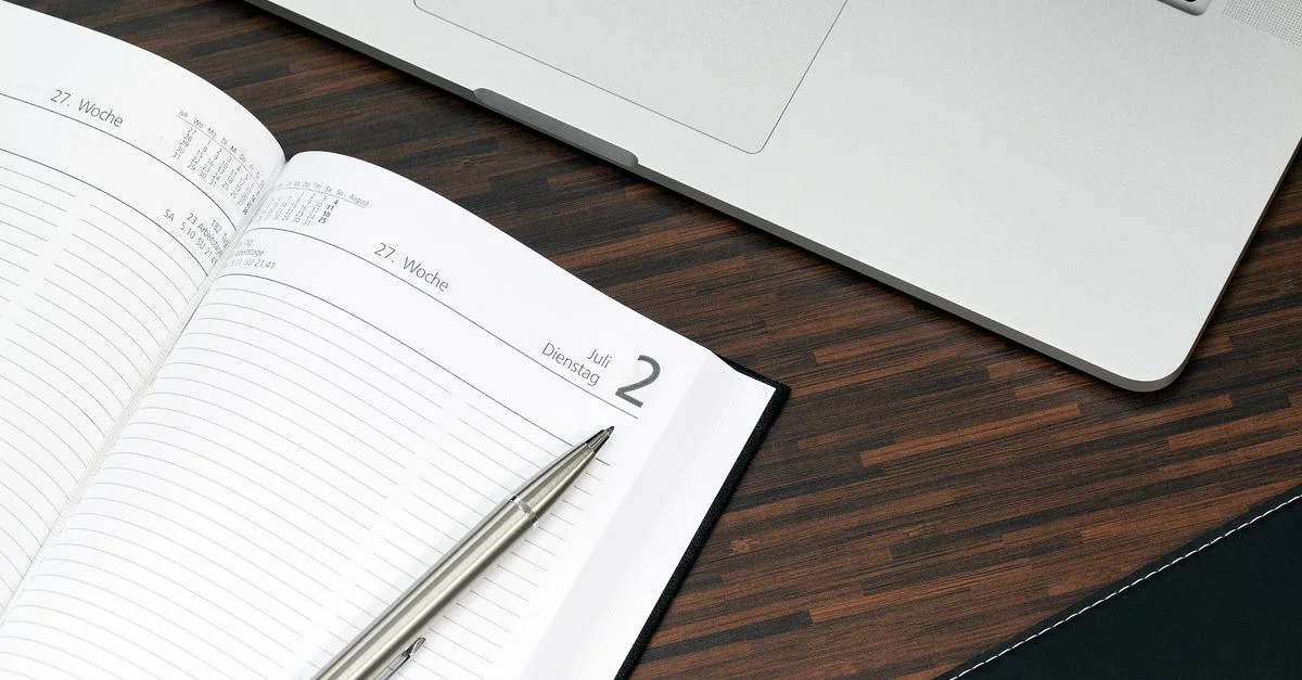 Planificateur ouvert avec un stylo et un ordinateur portable sur un bureau en bois, prêt pour l'organisation.